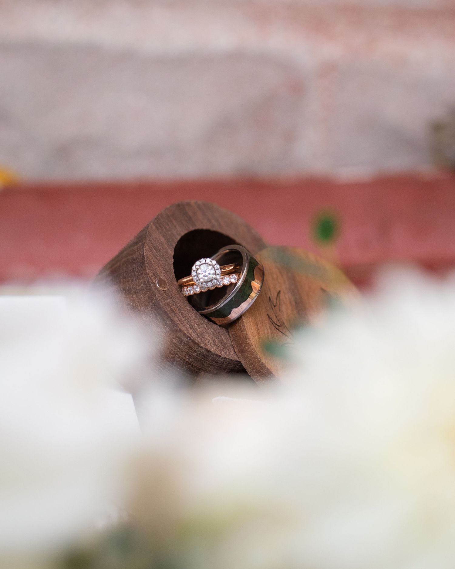 Wedding rings nestled in a rustic wooden detail with soft white floral accents.