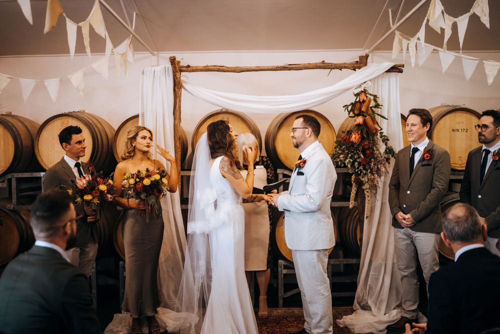 Wedding ceremony in progress with couple exchanging vows under rustic wooden arch and white draping.