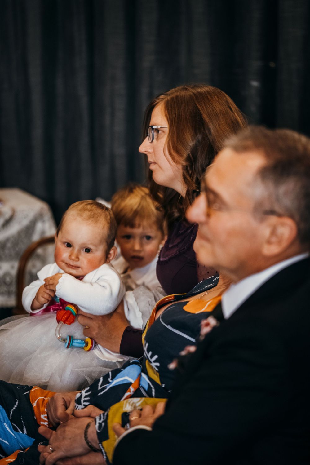 Wedding guests seated in formal attire watching ceremony with small children.