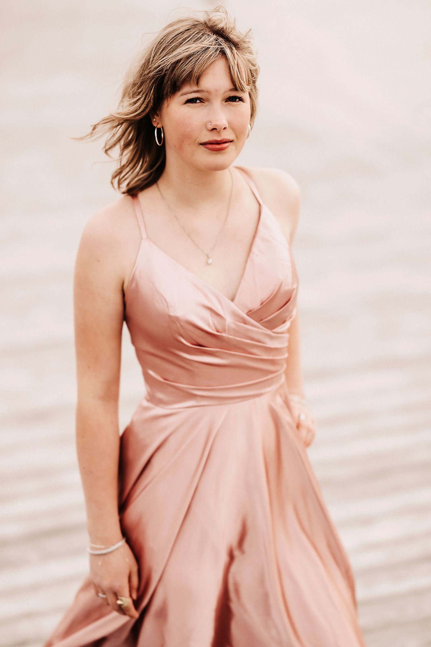 Portrait in flowing pink dress with wind-swept hair against neutral background.
