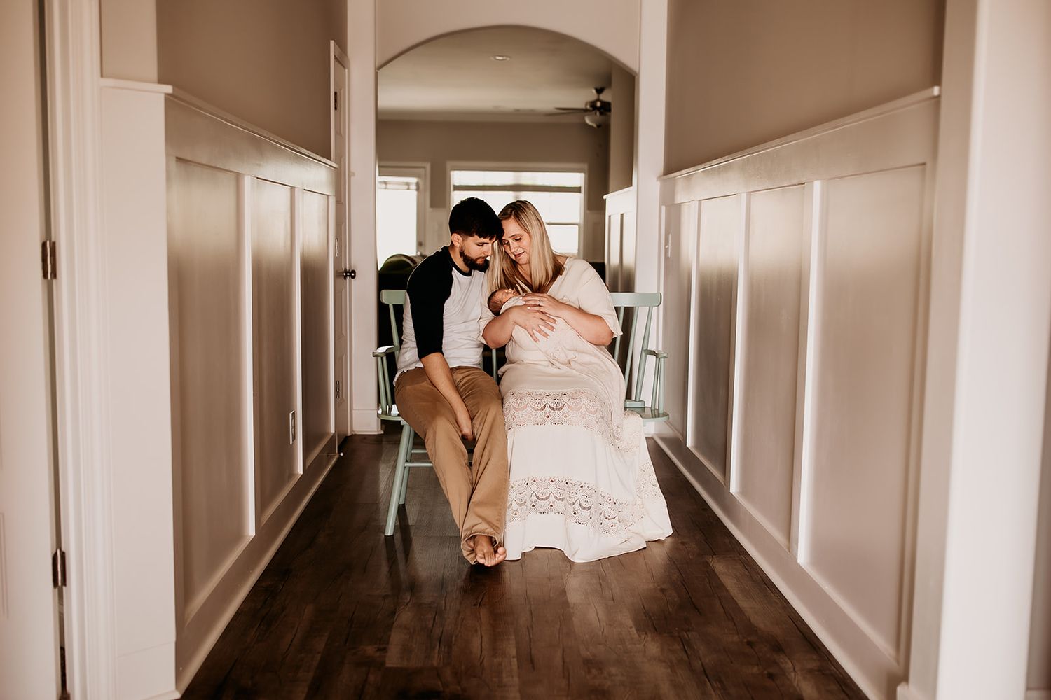 Parents sit on a bench in their entry way while holding their newborn son.