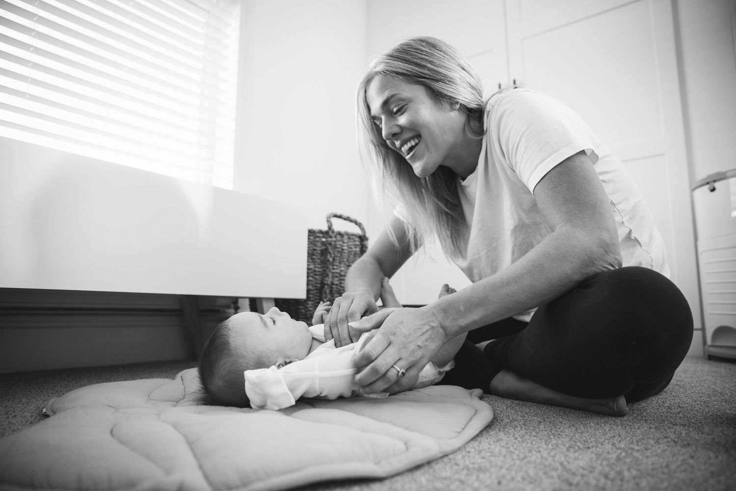 Black and white image of tender caregiving moment on carpet near window with natural light.