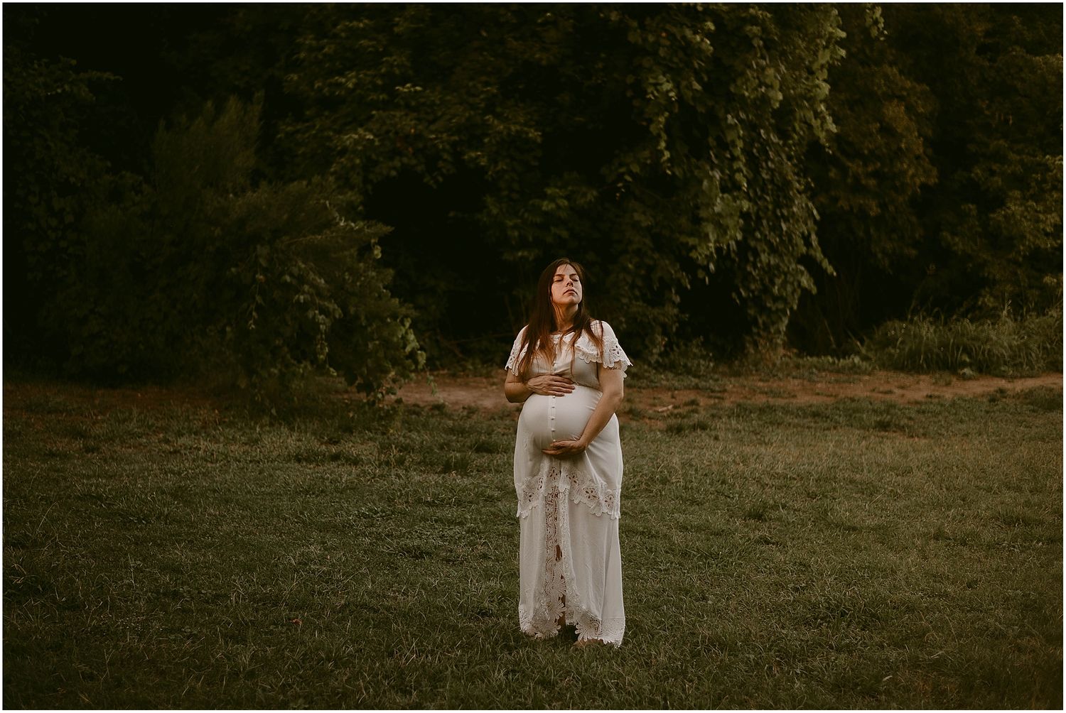 Romantic maternity portrait in a sunlit meadow featuring a flowing white lace dress.