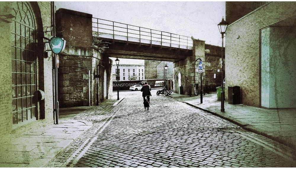 paul heaney photography man walking down cobbled street past brewdog bar towards railway viaduct bridge in leeds