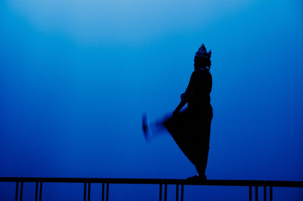 Silhouette figure standing against deep blue background on elevated platform.