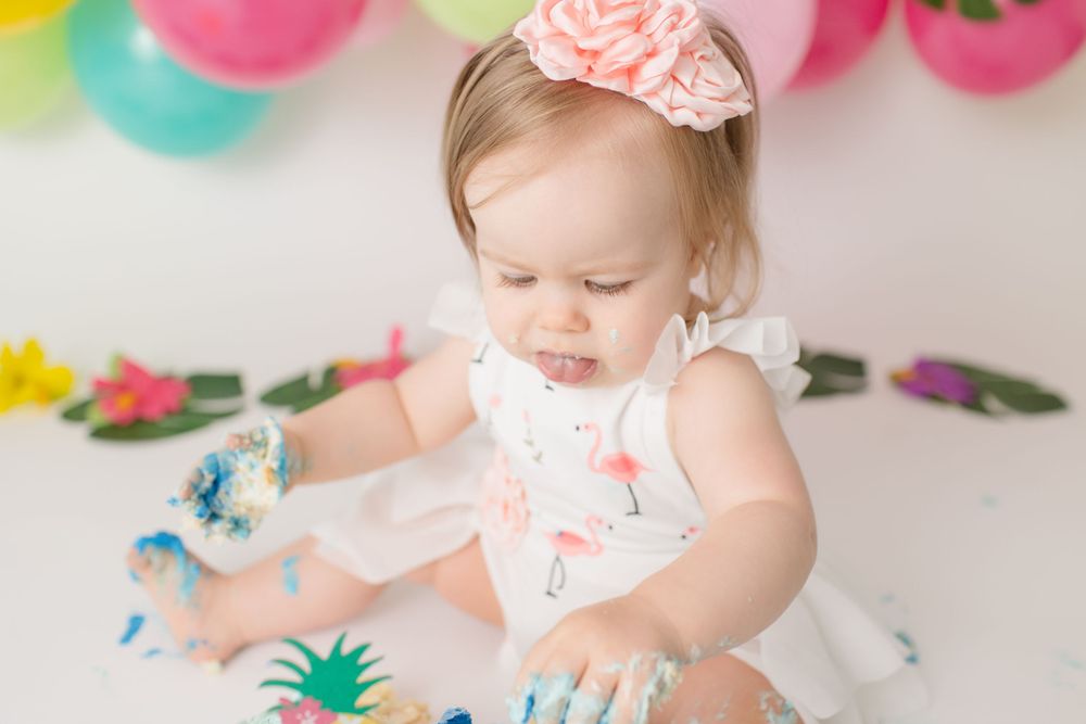 A cake smash photoshoot with pink bow and tropical decorations.