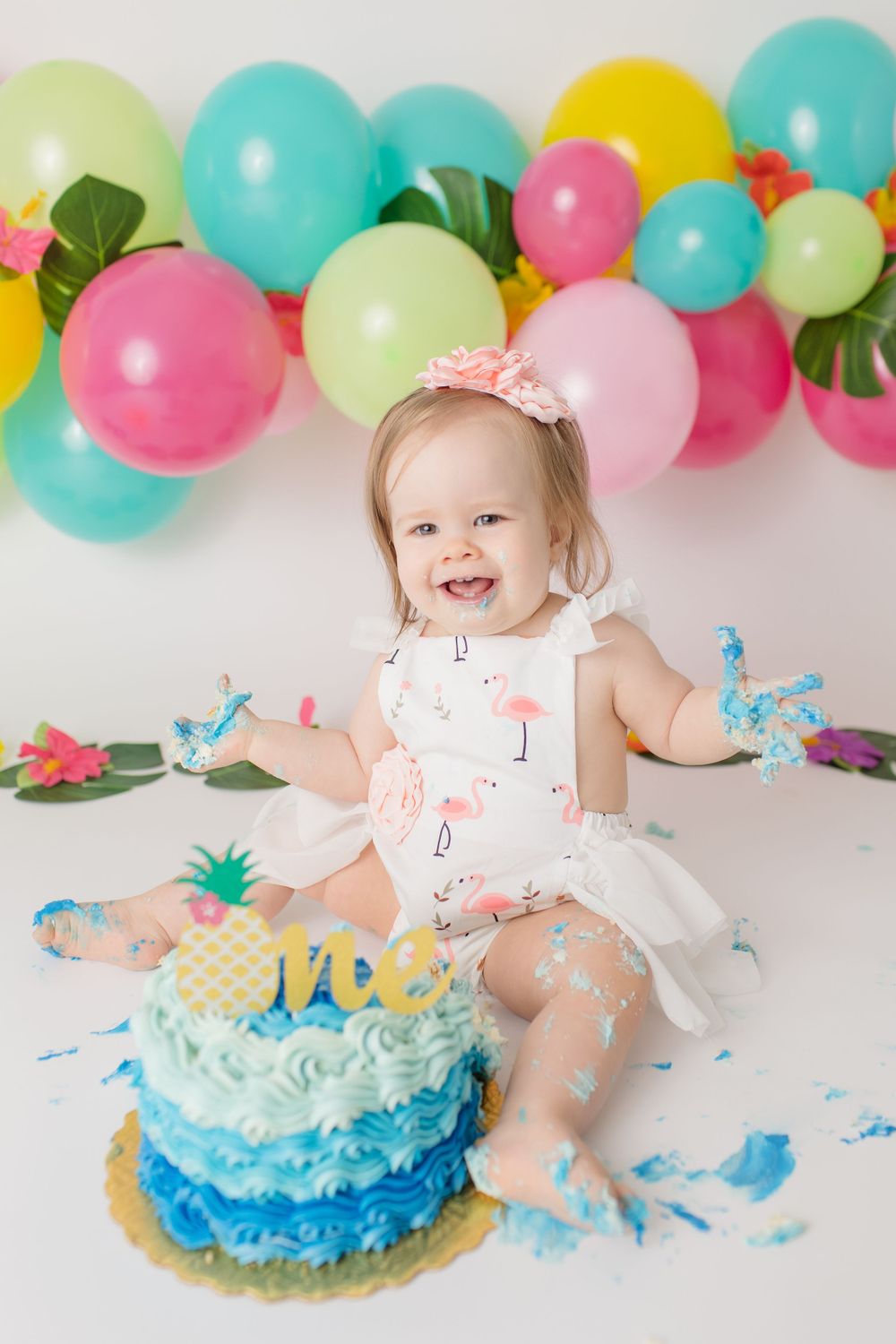 First birthday cake smash with tropical themed decorations and colorful balloon arch.