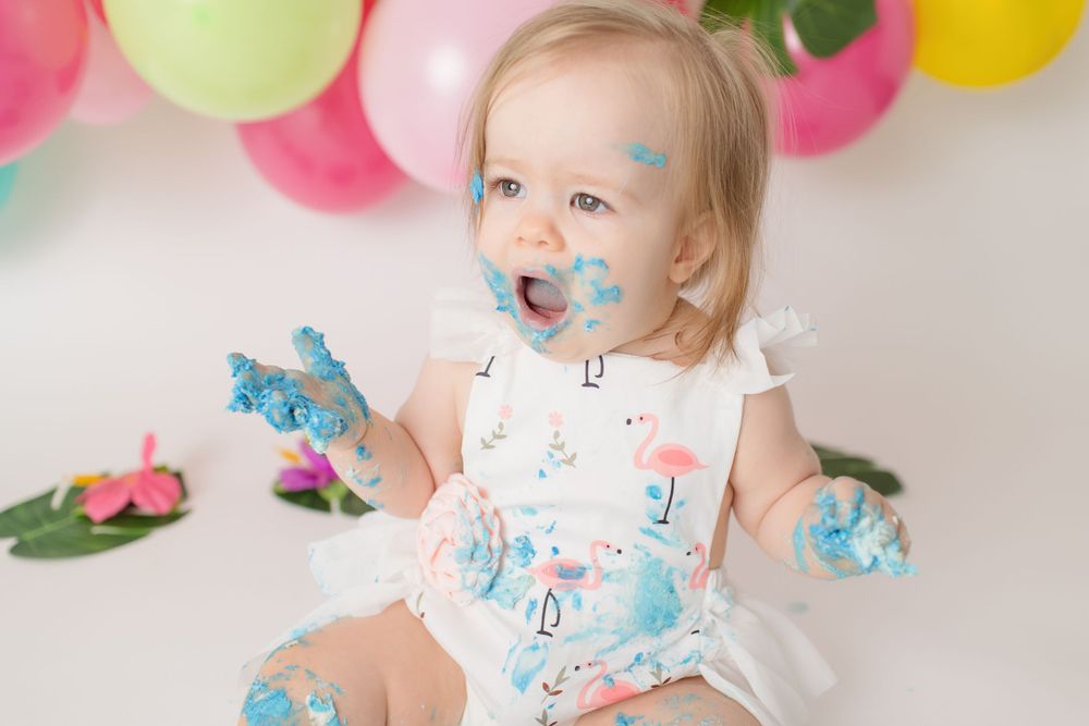 Messy cake smash photo with blue frosting and floral outfit.