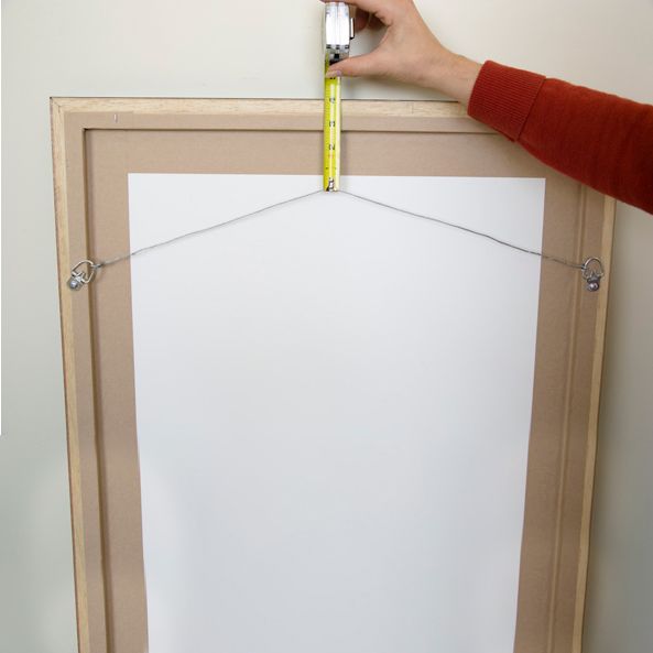 Demonstration of measuring proper picture frame hanging height with tape measure.