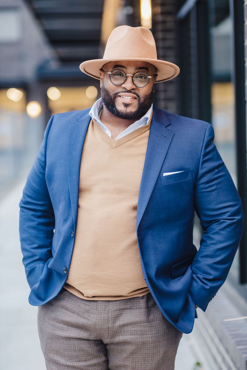 Stylish professional in blue blazer, tan hat and sweater poses confidently.