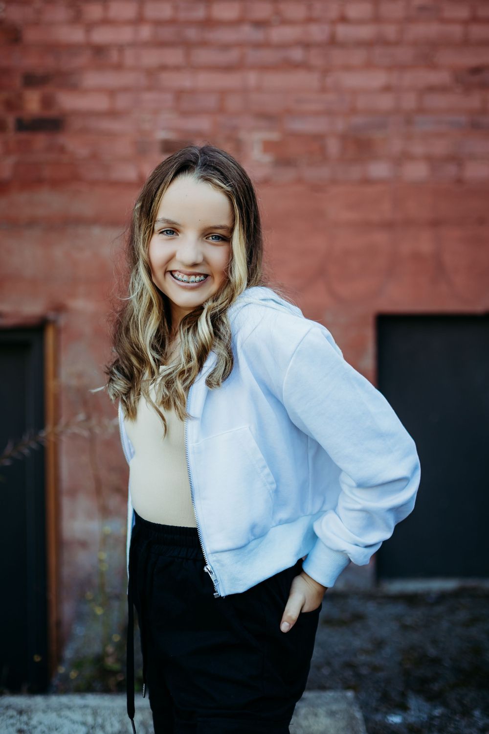 Stylish young person in light blue jacket and dark skirt poses against brick wall.