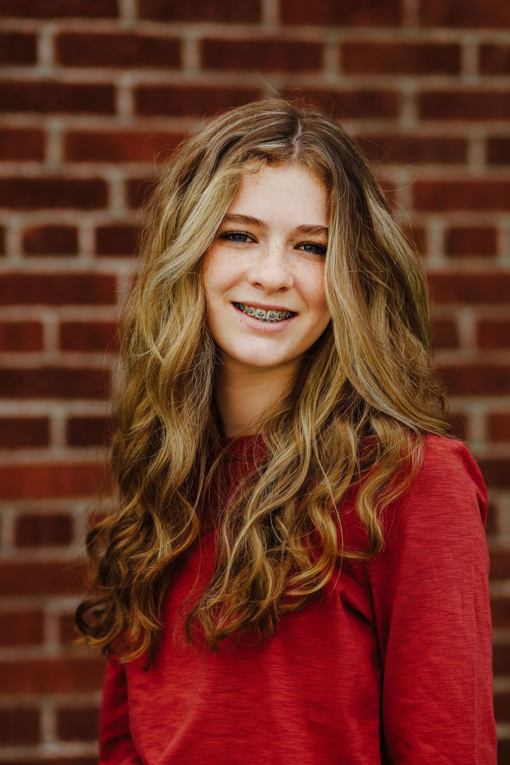 Portrait of young woman in red sweater smiling against brick wall background.