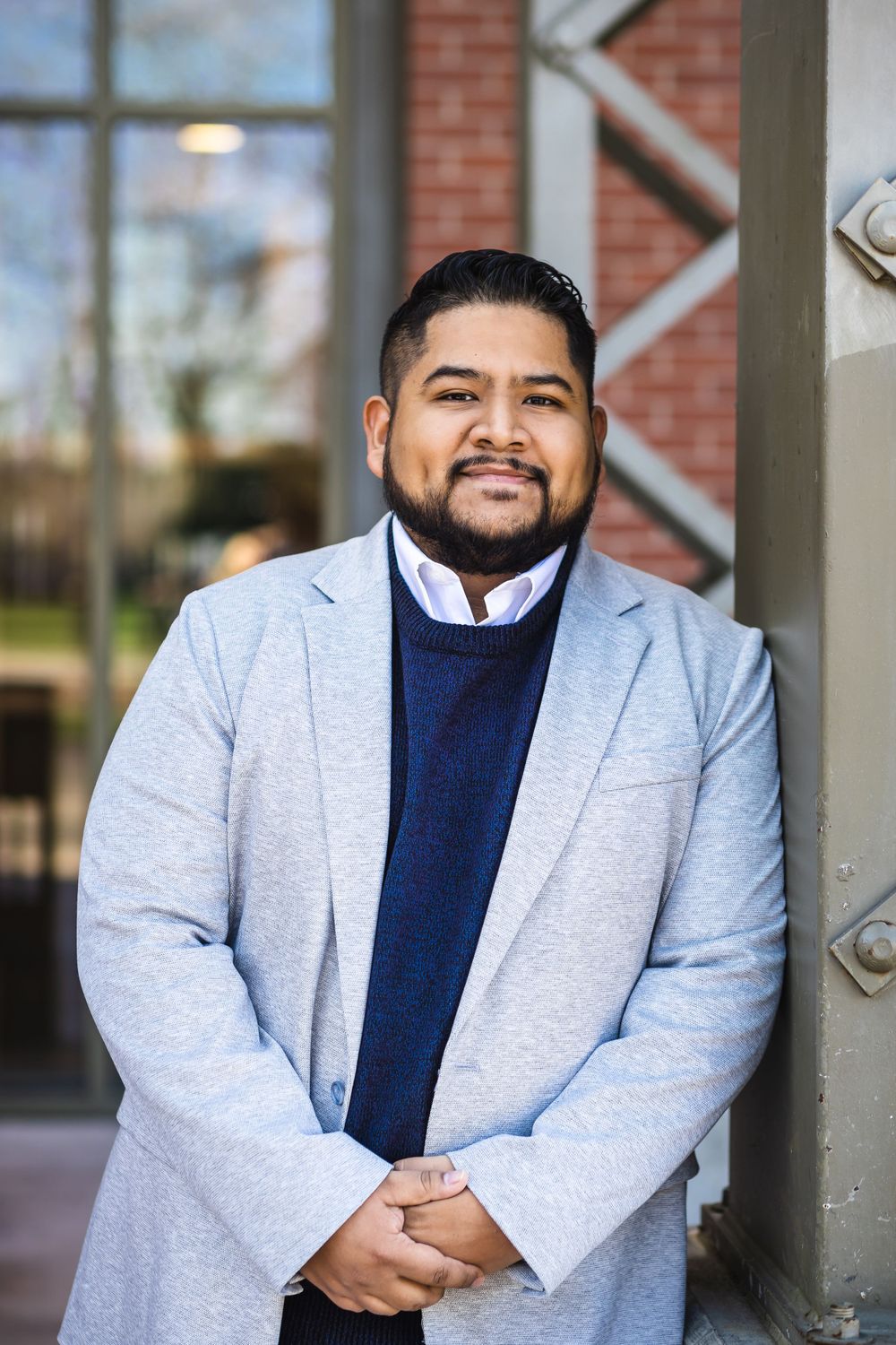 Professional wearing light gray blazer and navy sweater poses confidently by building entrance.
