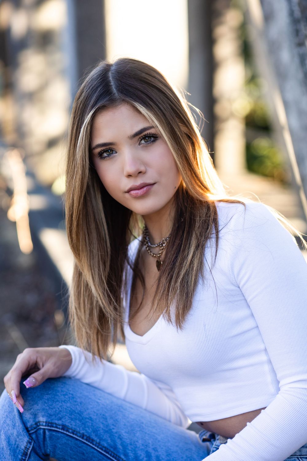 Young woman in a white long sleeve crop top and jeans poses outdoors with soft natural lighting.