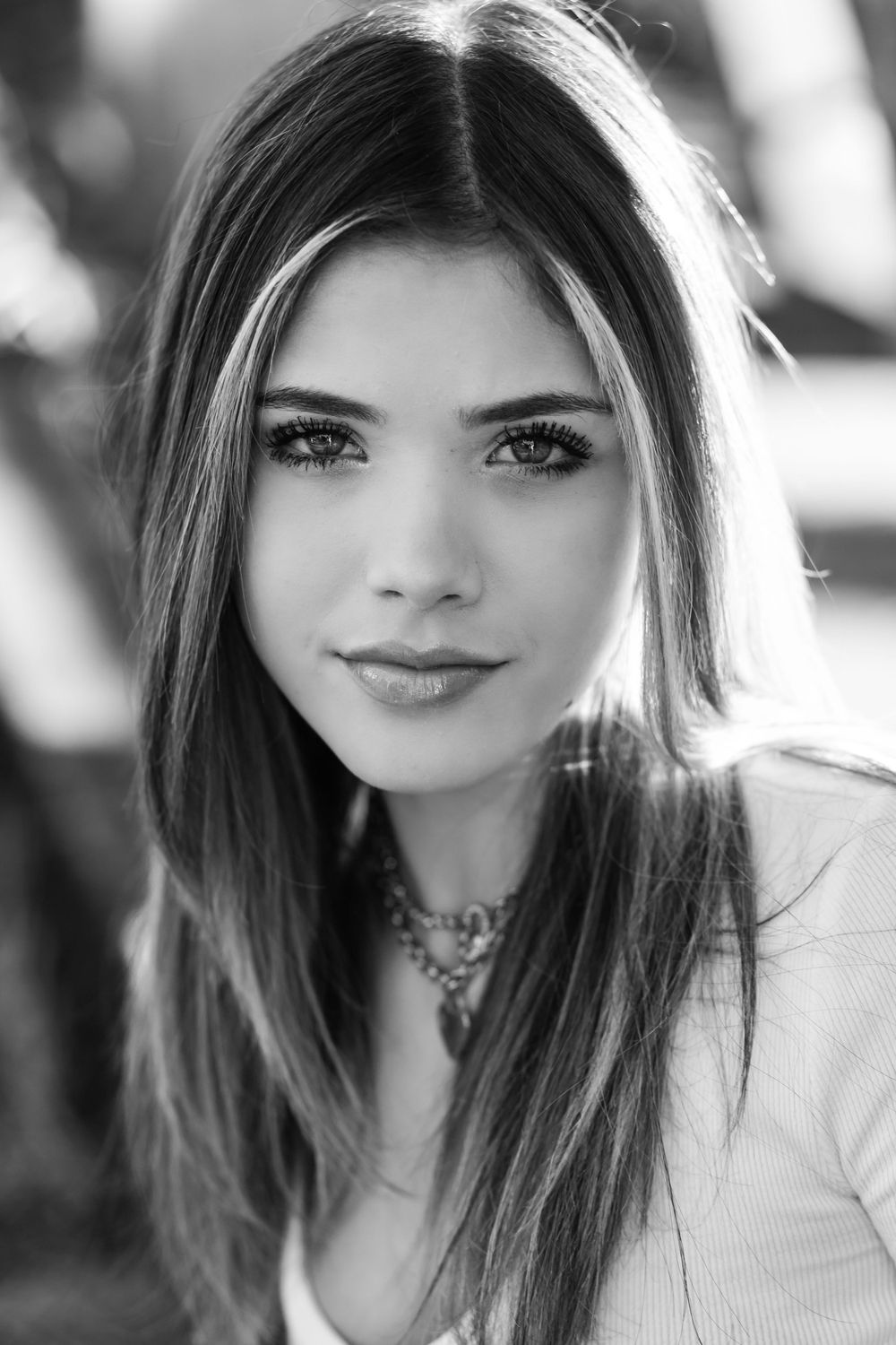 Portrait of a woman with long brown hair wearing a white top and necklace in black and white.