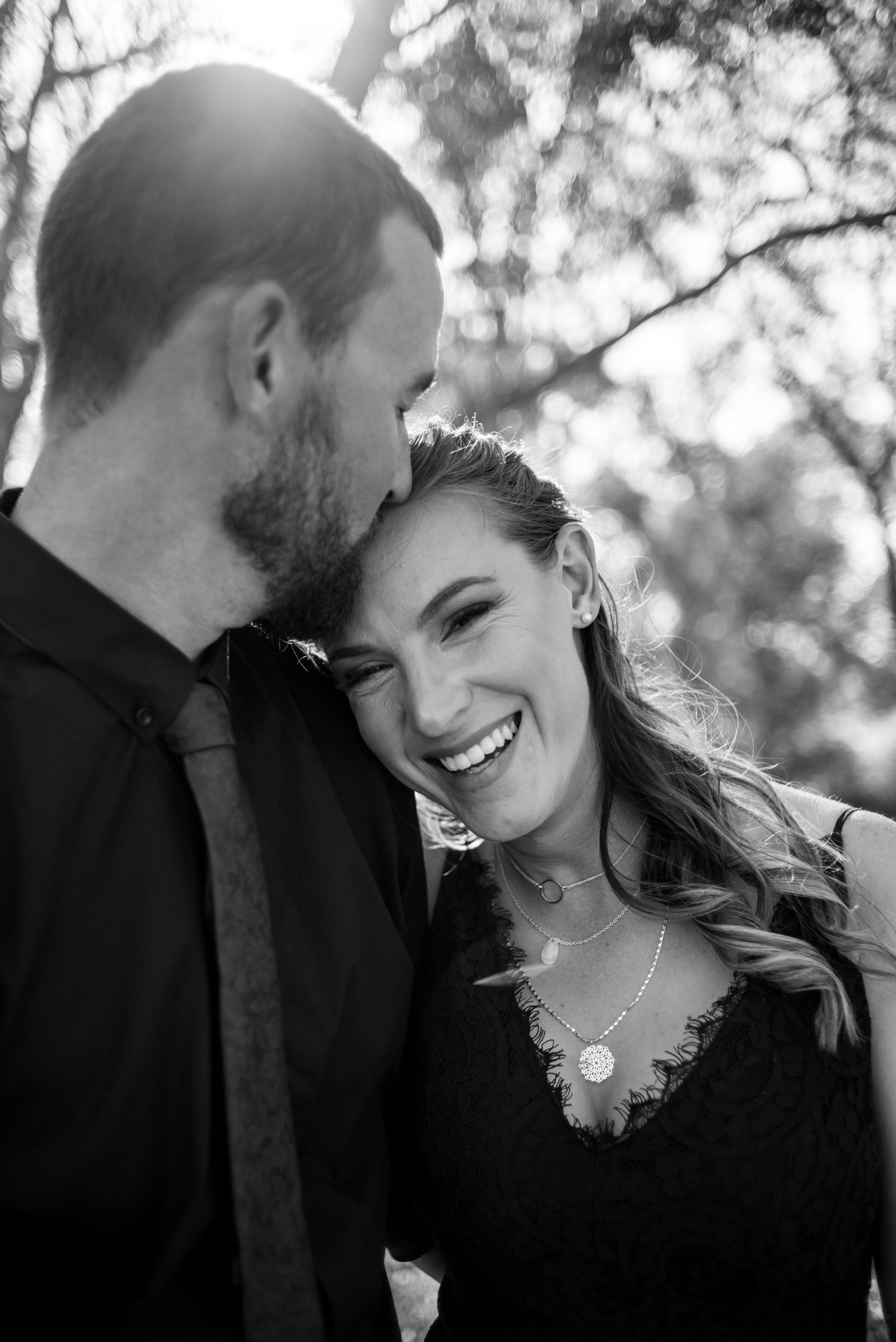 An intimate black and white portrait of a couple sharing a joyful moment outdoors.