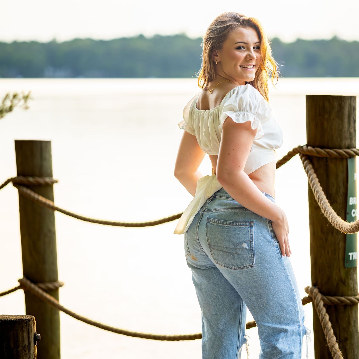 Lifestyle portrait by waterfront dock featuring casual denim and summer top.