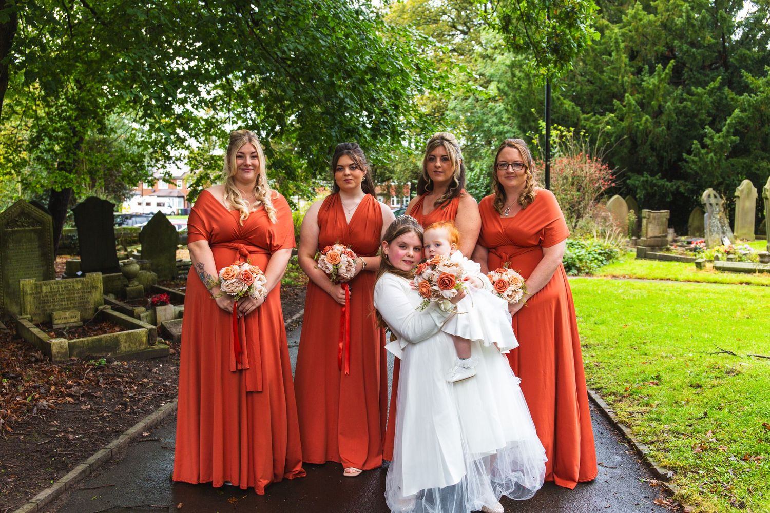Wedding party in coral dresses poses together on a garden path.