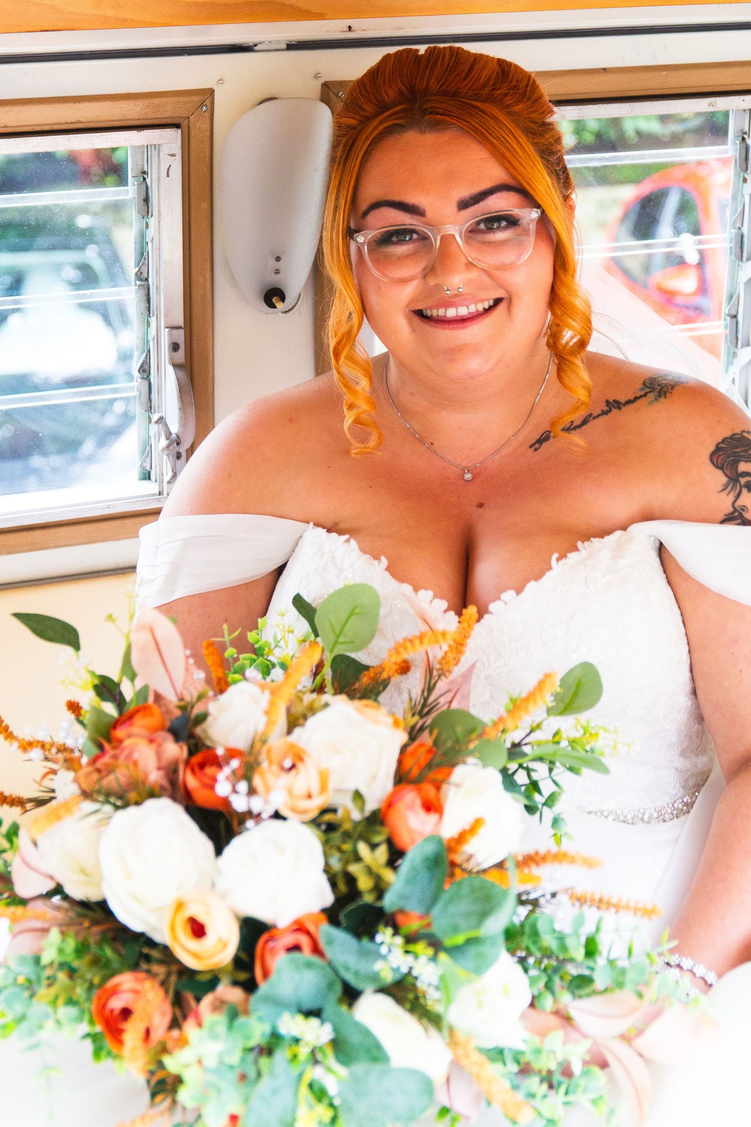 A bride in a white dress holds a vibrant orange and white floral bouquet inside a vintage vehicle.