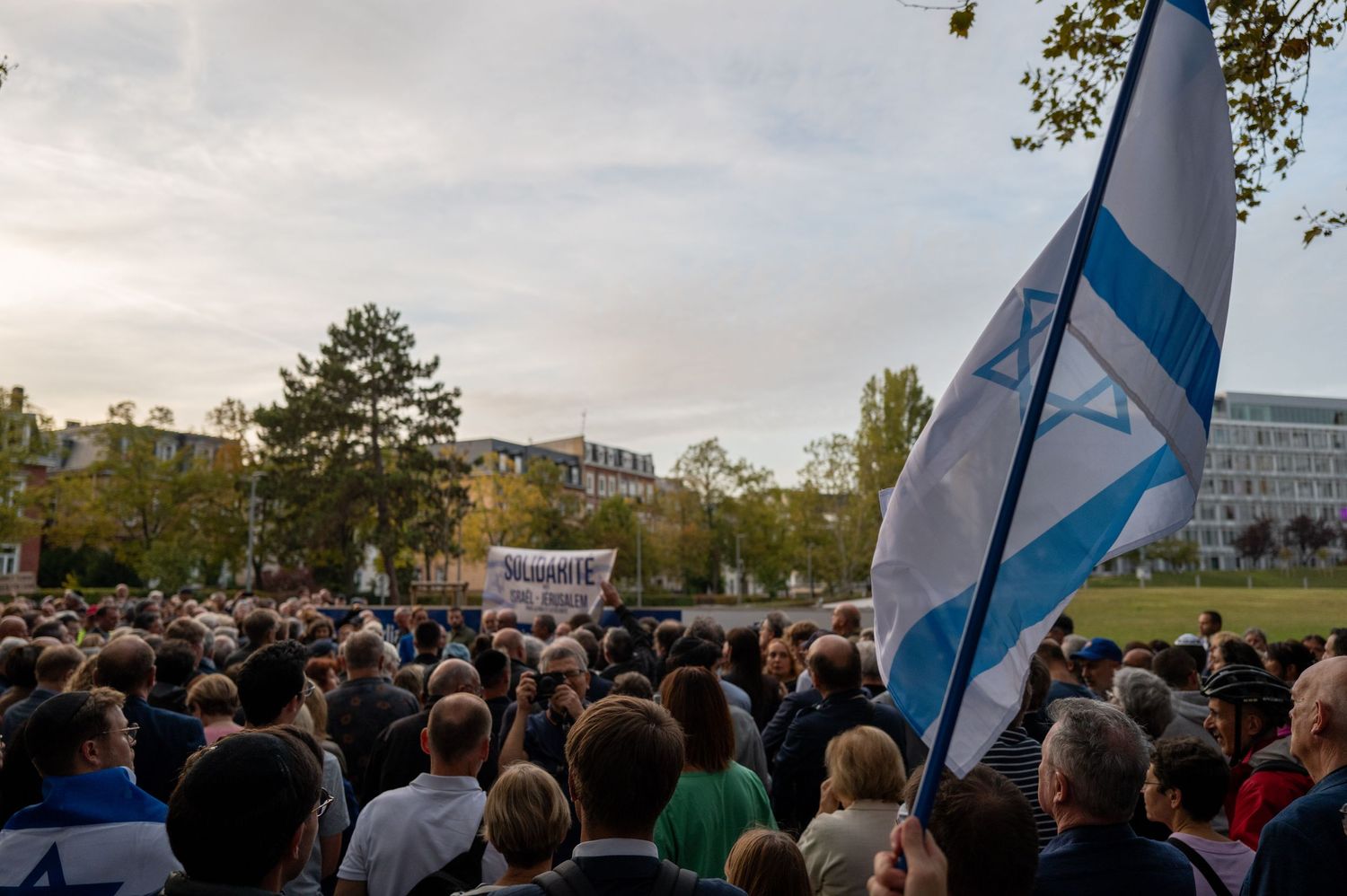 Large crowd gathered outdoors with flag visible against evening sky.