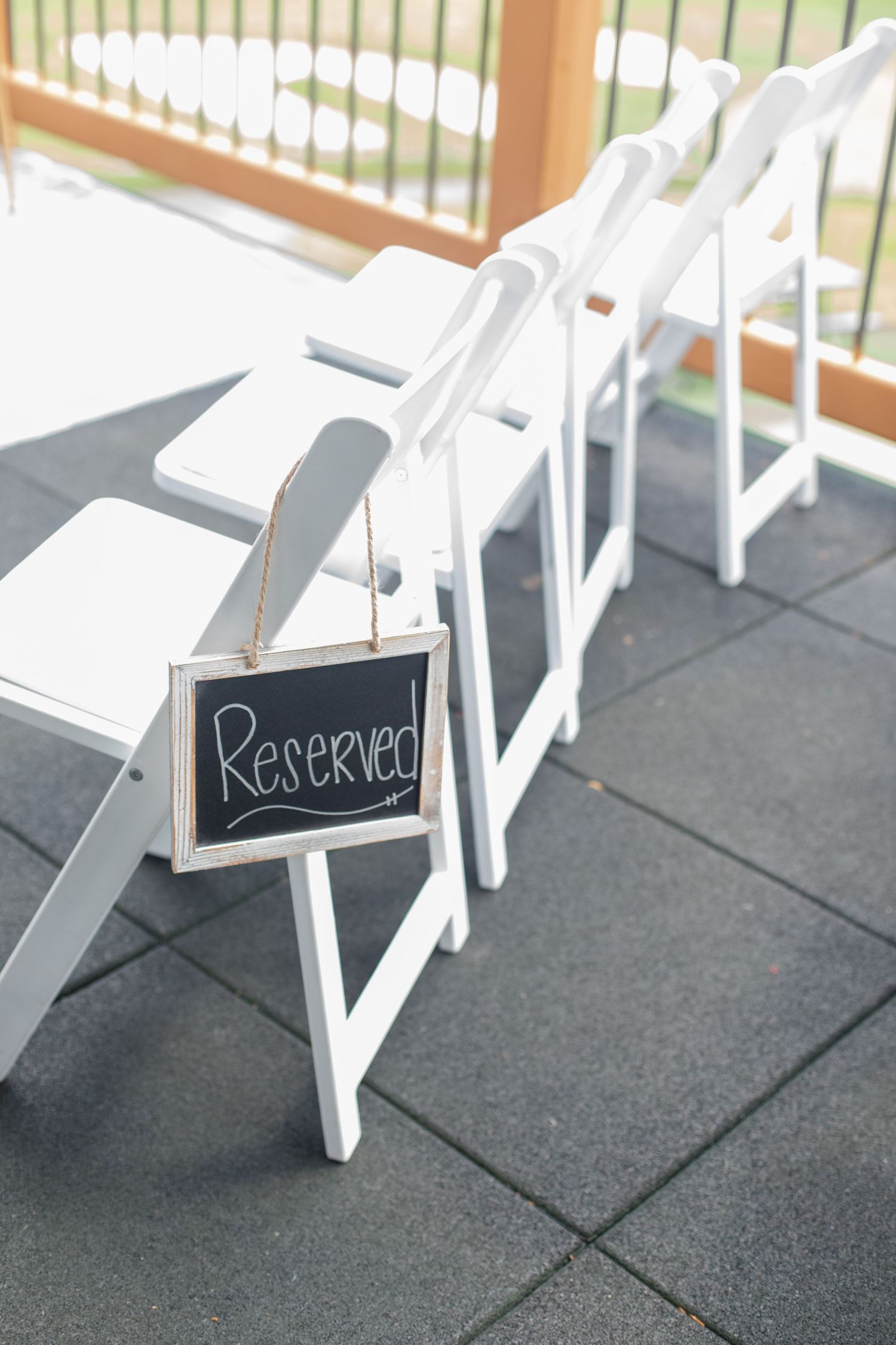 White folding chairs with small chalkboard signs arranged for a wedding ceremony.