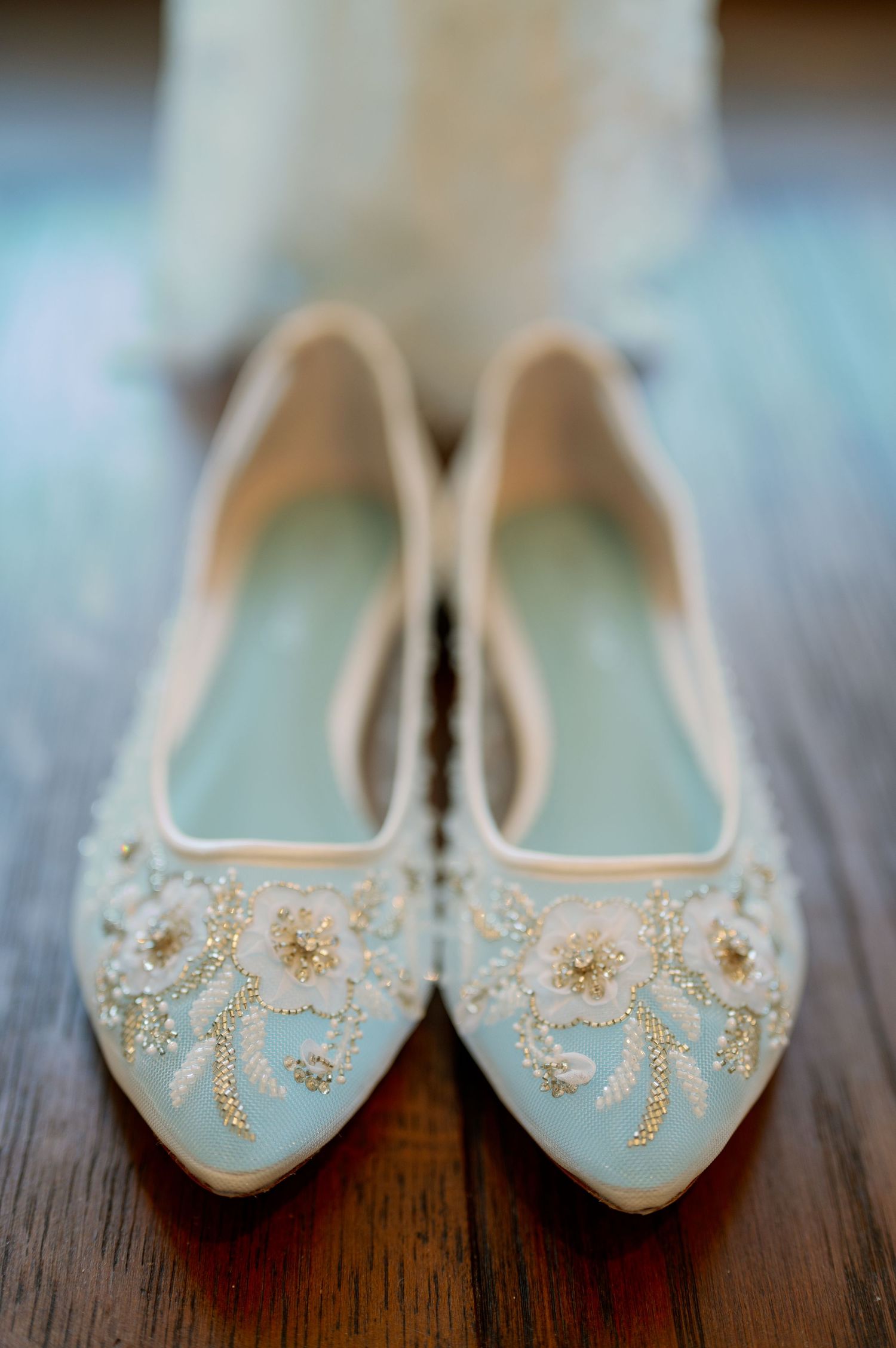 Pale blue ballet flats with gold beaded floral embellishments on wooden floor.