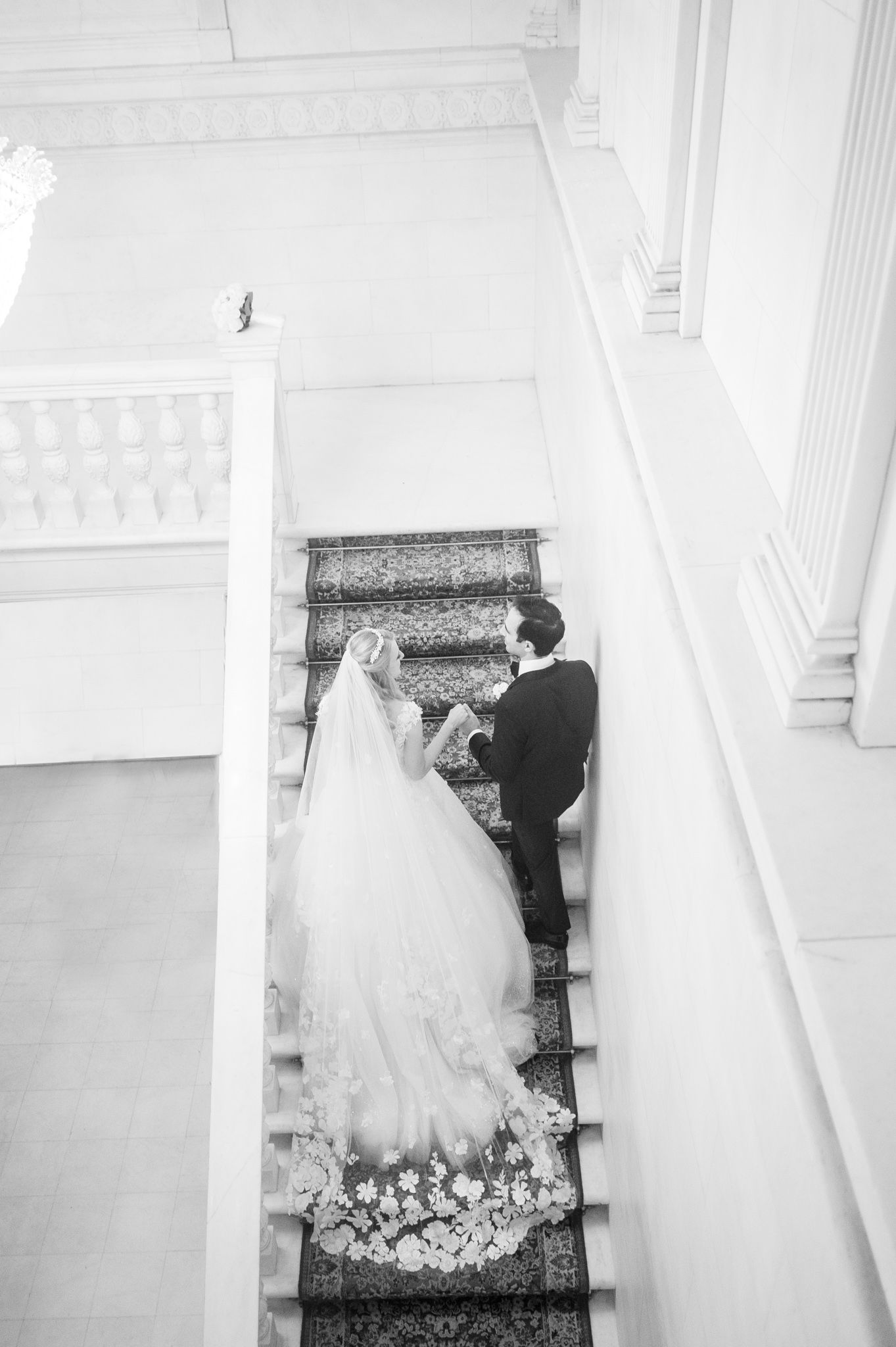 Couple ascending NYIT's staircase with the bride's dress, long train, and veil fully displayed.