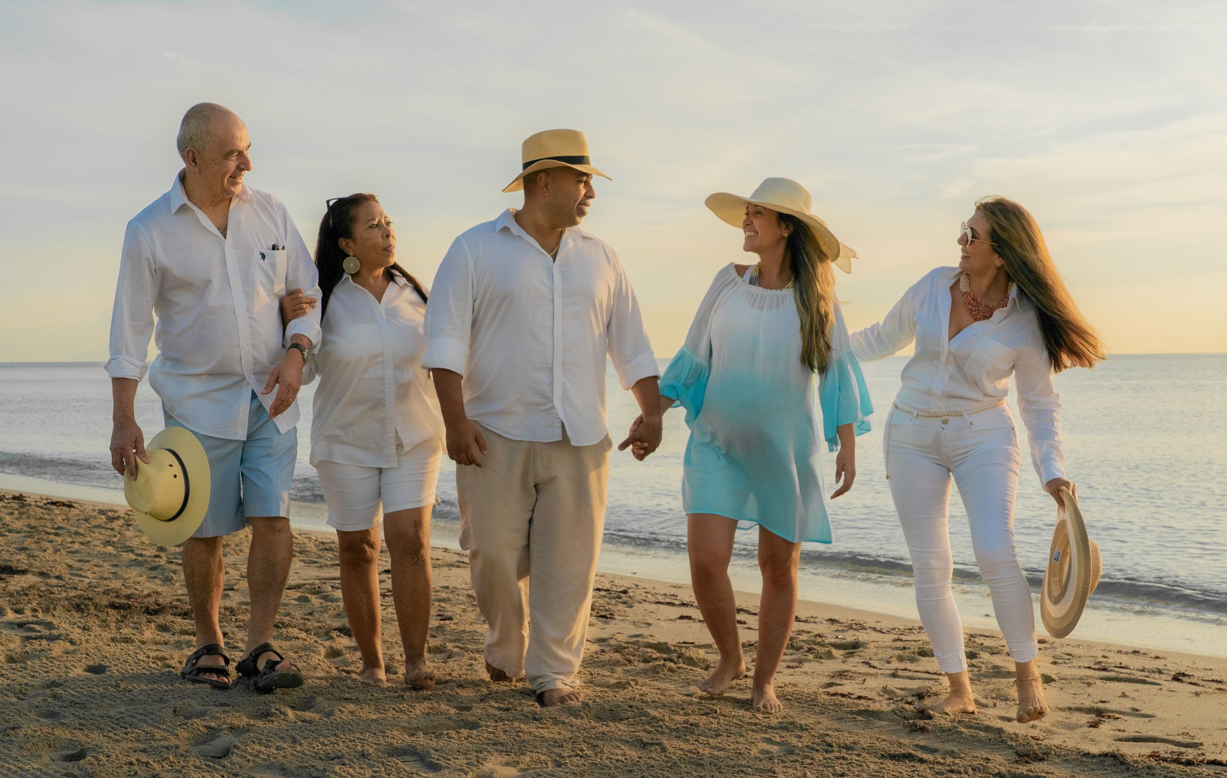 Happy family of five walking together on sandy beach at golden sunset in white outfits.