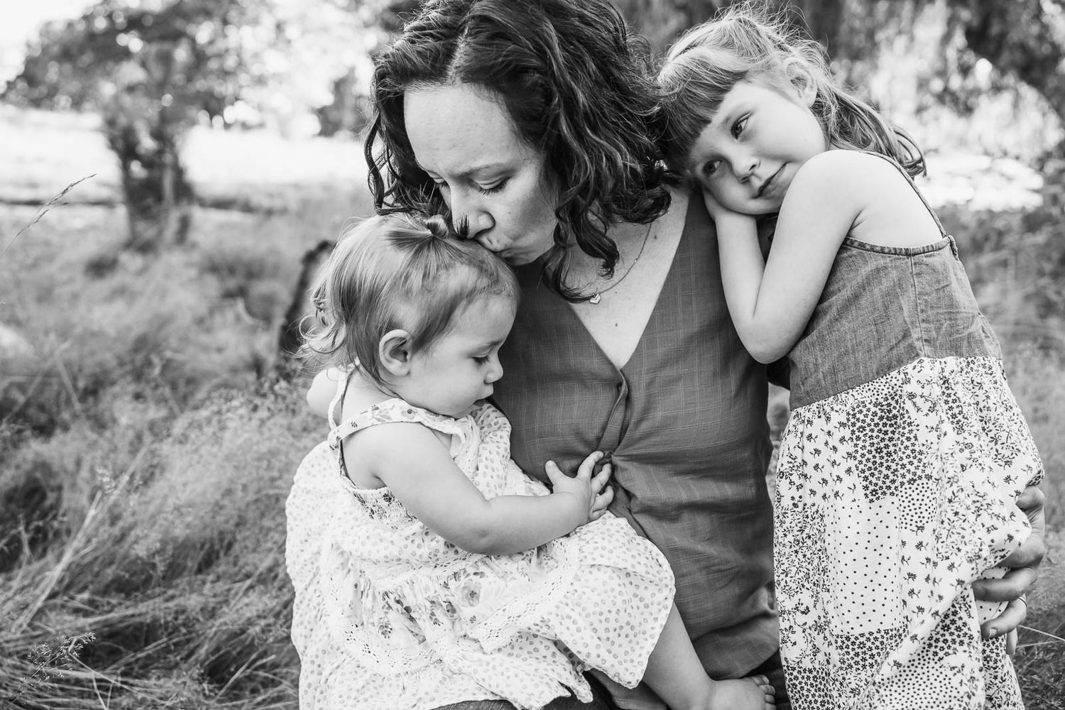 Black and white image of mother hugging and kissing her children.