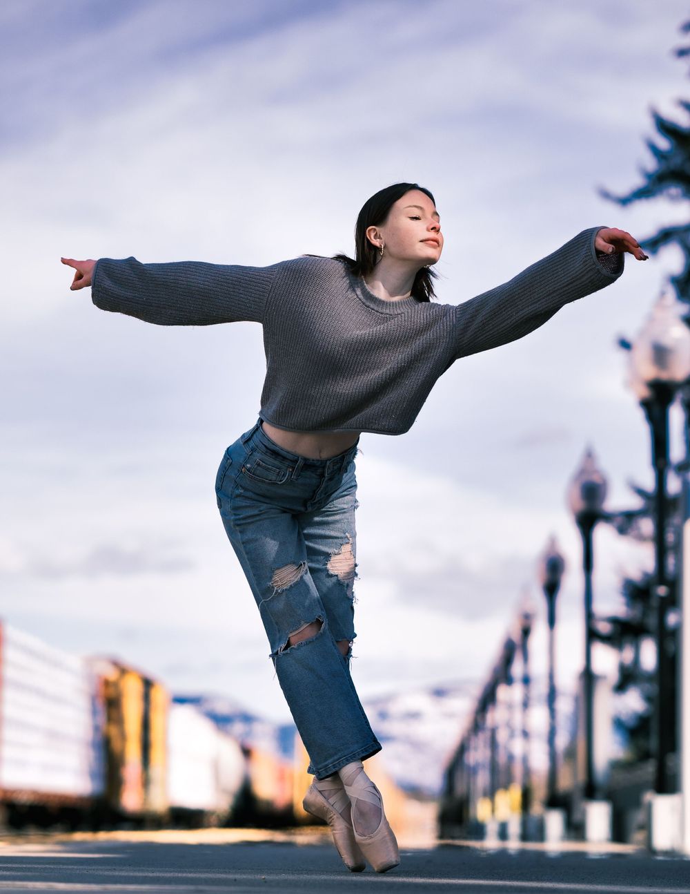 Dancer balances on pointe shoes with outstretched arms against an urban cityscape.