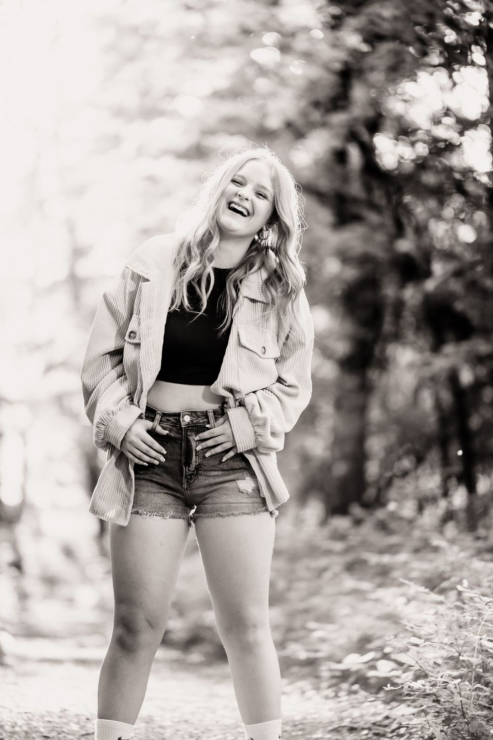 Black and white portrait of a joyful person in denim shorts and jacket laughing outdoors.