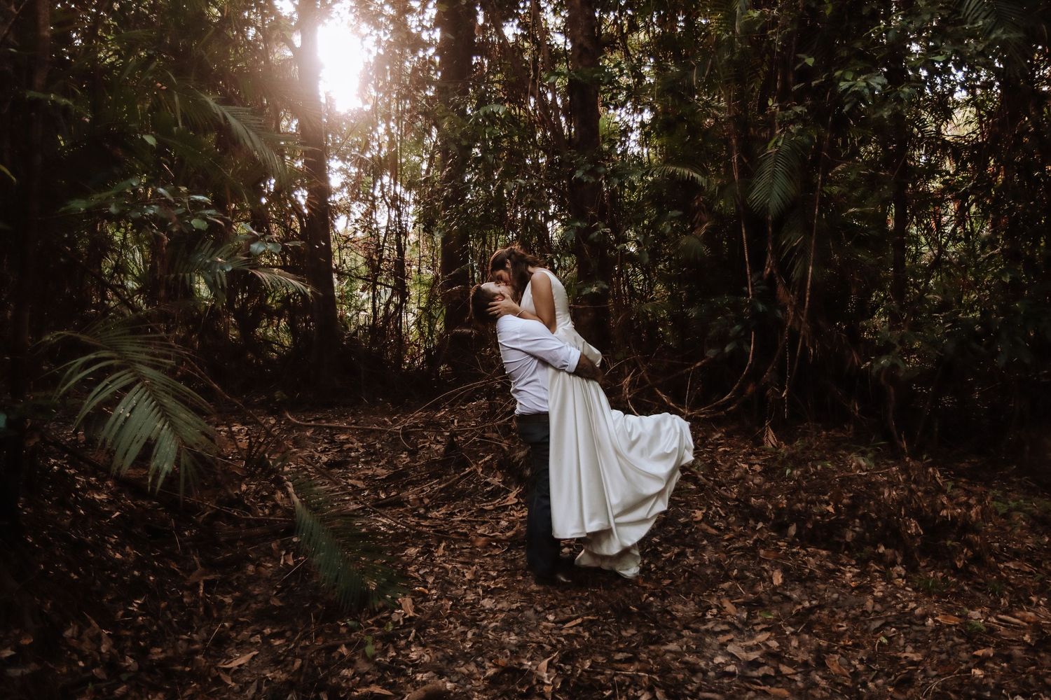 A romantic wedding portrait of a couple in white attire surrounded by lush forest greenery.