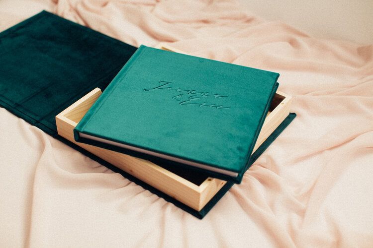 Emerald green velvet wedding albums stacked on cream colored fabric.