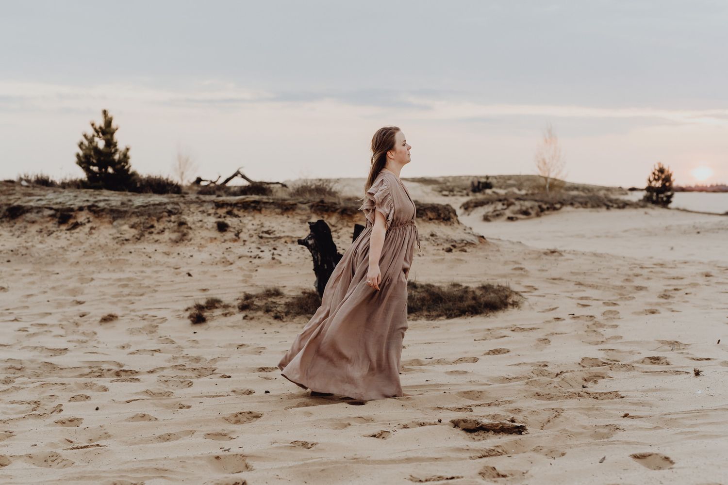A flowing dress catches the wind on a sandy beach landscape at dusk.