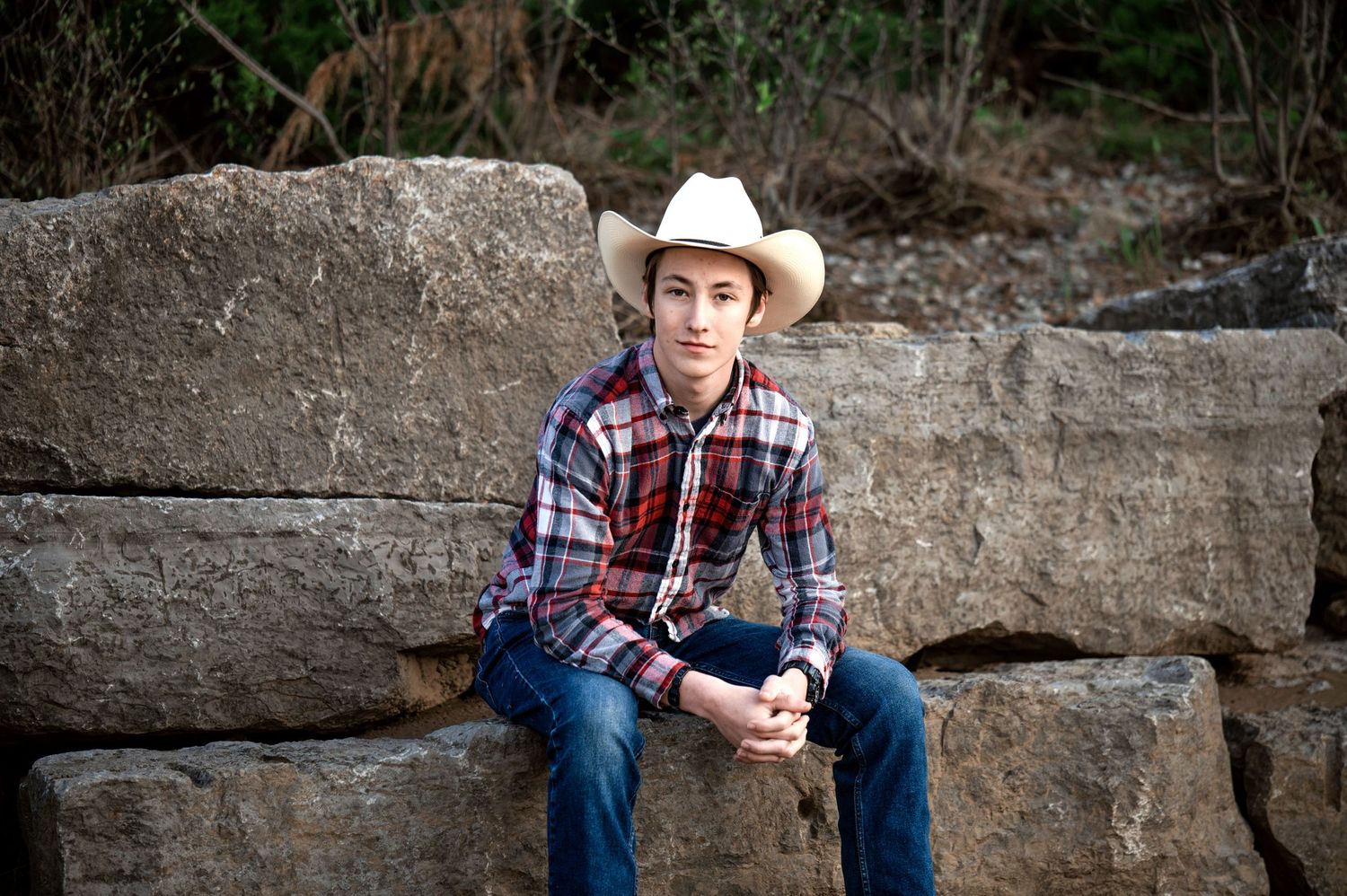 Senior portrait of teen in western wear sitting on stone ledge.