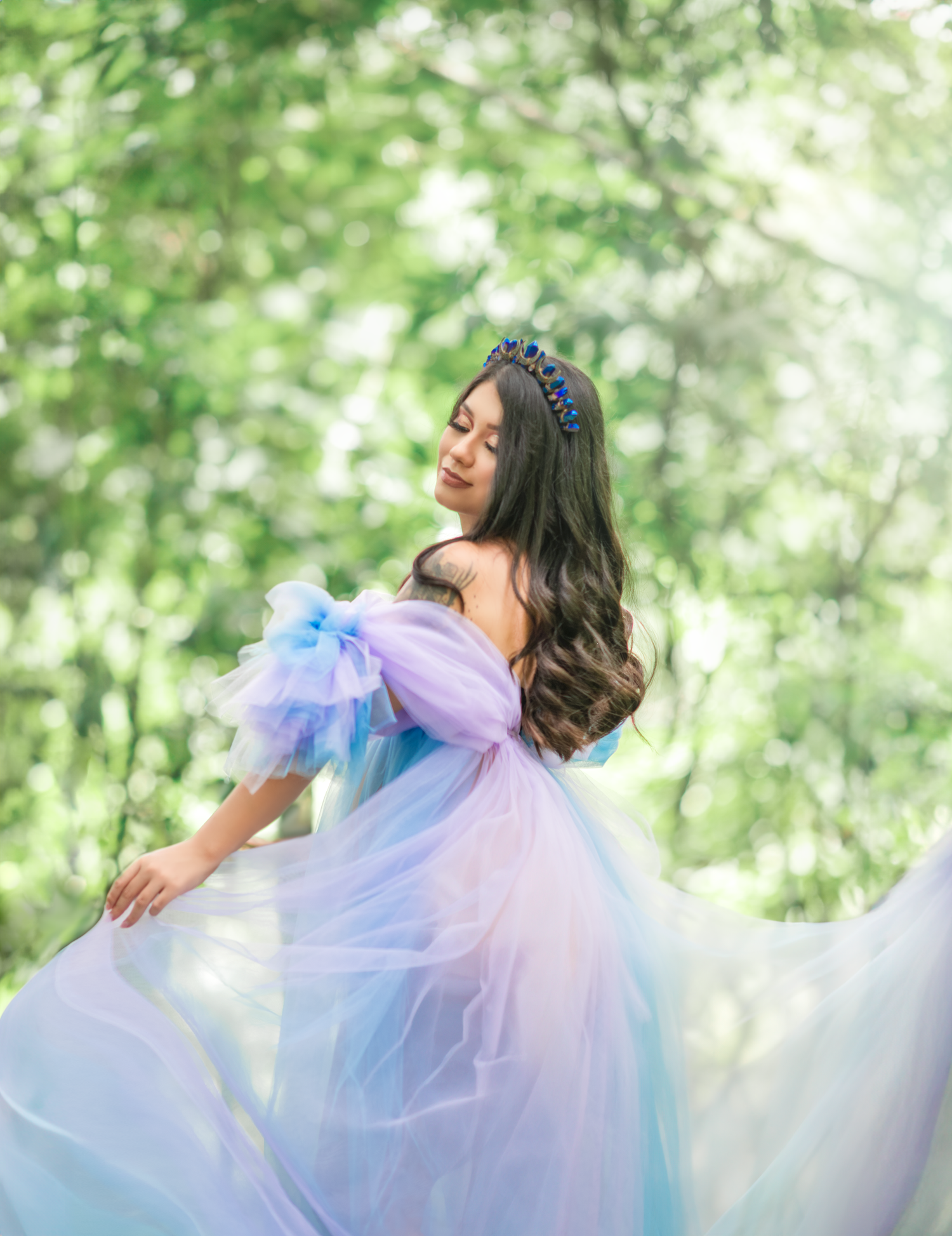 Ethereal portrait in flowing pastel dress with floral crown against green nature backdrop.
