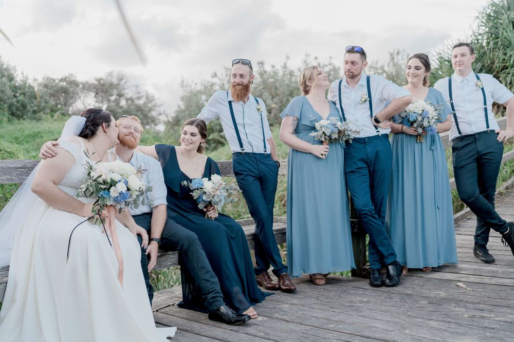 plus size wedding party in shades of blue laughing and smiling on park seats under cloudy sky