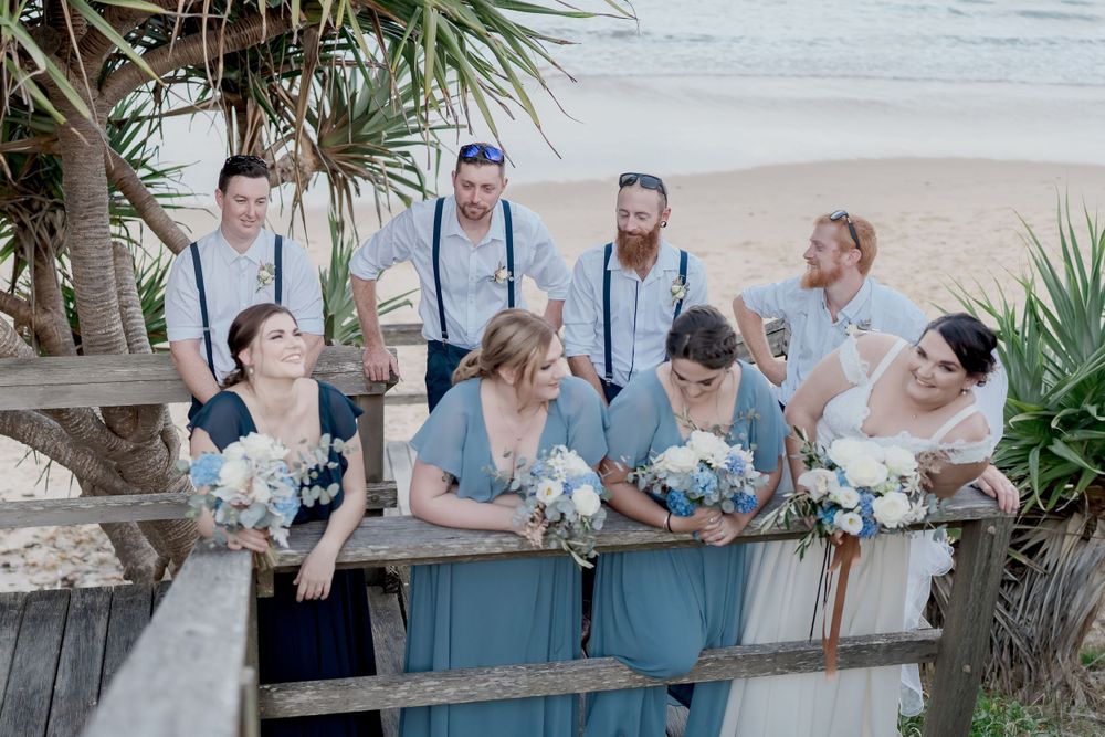 wedding party in shades of blue grouped on boardwalk above sandy ocean beach