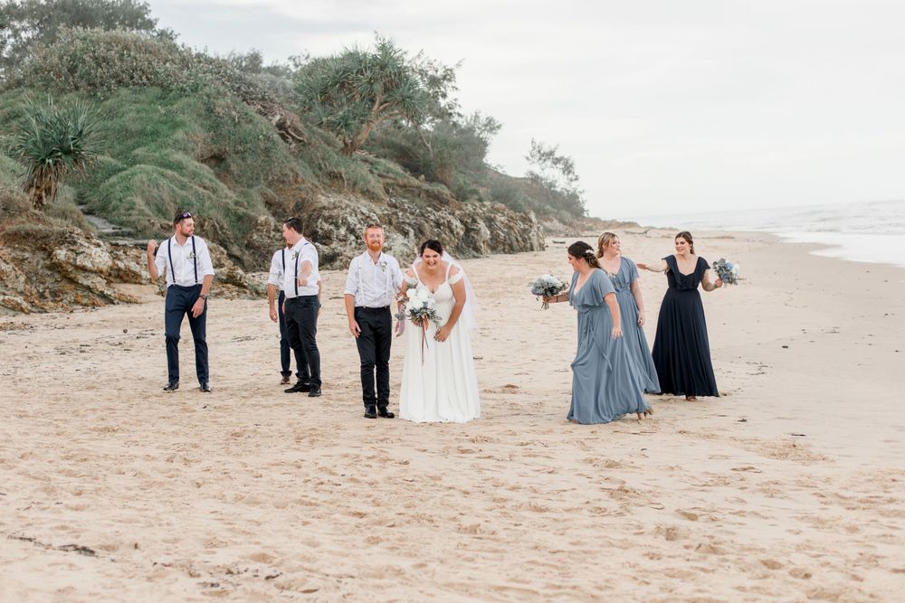 wedding party in shades of white and blue walking on beach in stormy weather