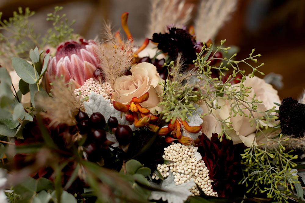 Close-up of moody wedding floral arrangement with protea, roses and delicate greenery.