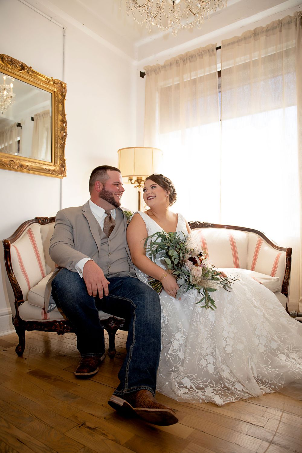 A couple shares a joyful moment while seated on an antique sofa in an elegantly decorated room.