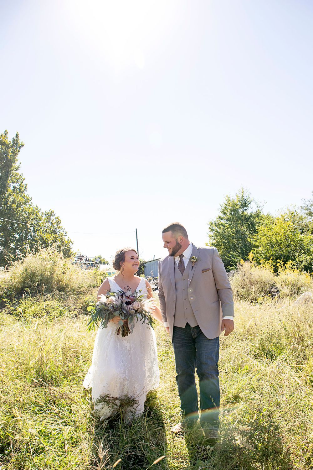 A couple shares a candid moment while standing in a sunlit field of tall grass.