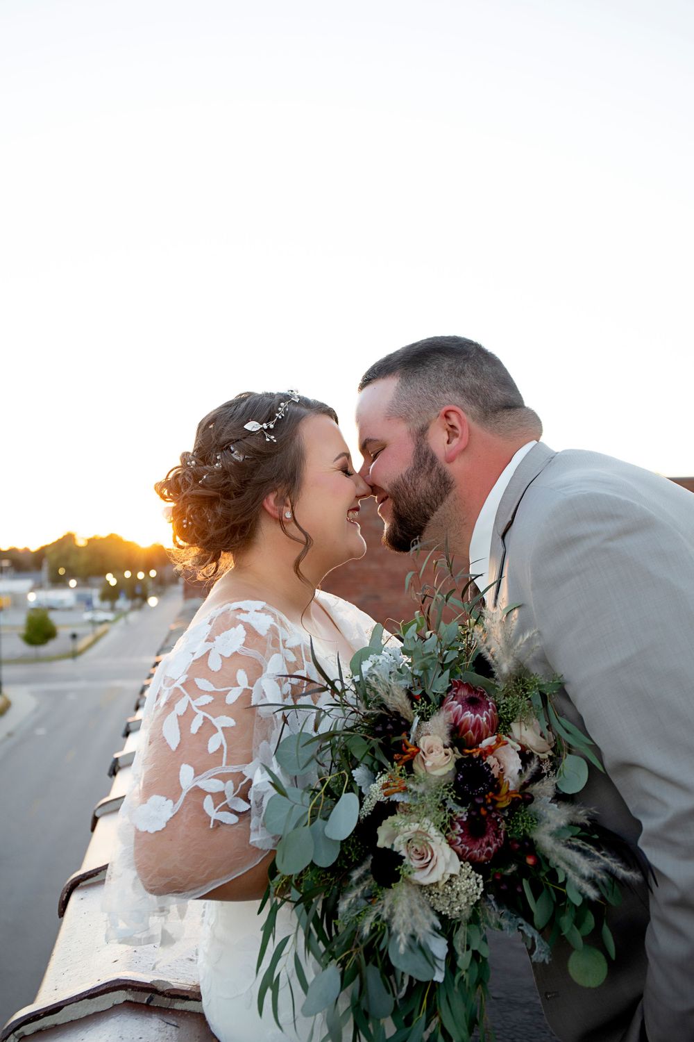 A romantic moment shared with a lush green and white bouquet against a bright sky.