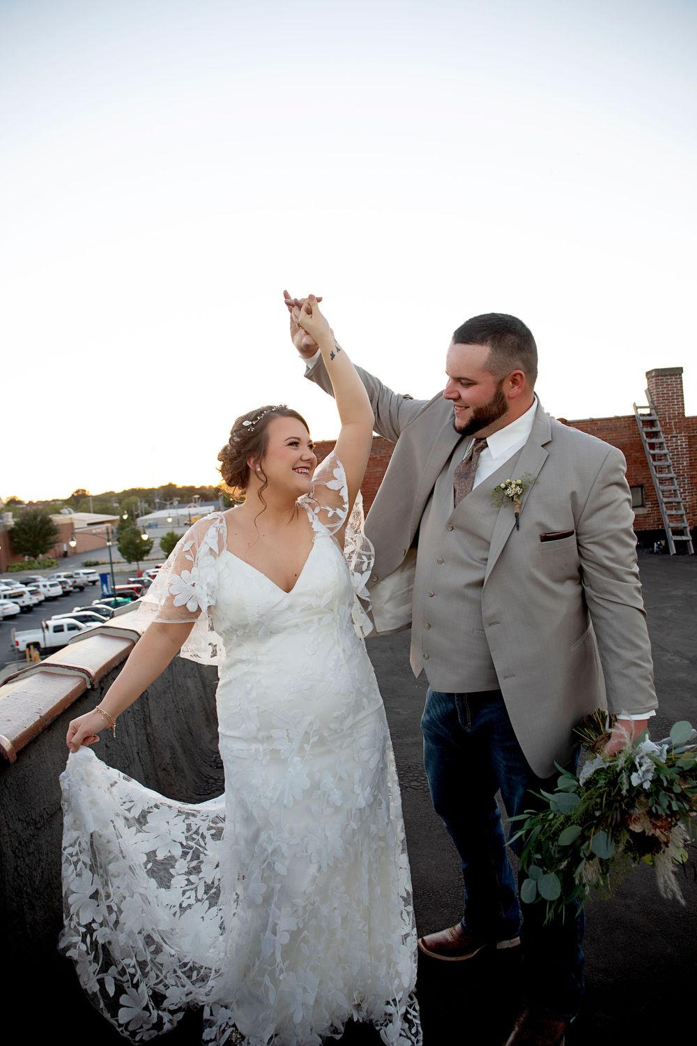 A joyful dancing moment captured on a rooftop during sunset with urban backdrop.