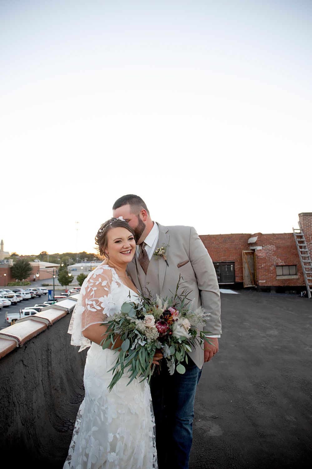 A wedding couple embraces on an urban rooftop with a beautiful floral bouquet.
