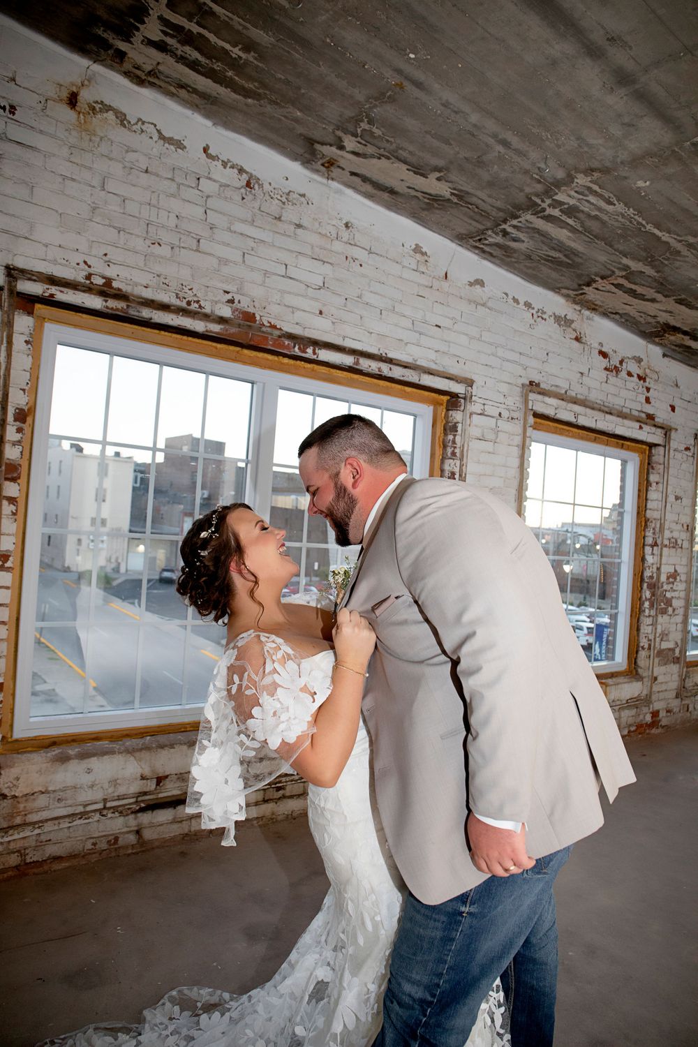 A romantic moment between newlyweds in an industrial loft space with exposed brick and windows.