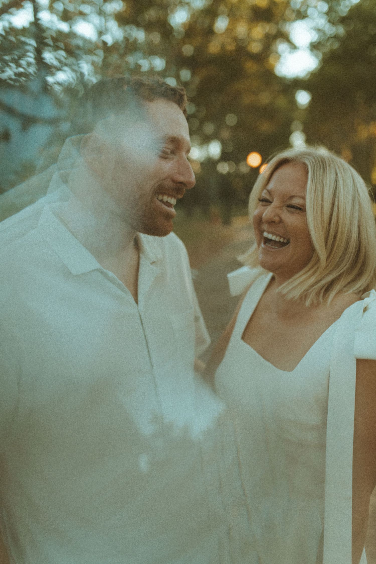 A joyful couple laughs together during a golden hour photoshoot outdoors.