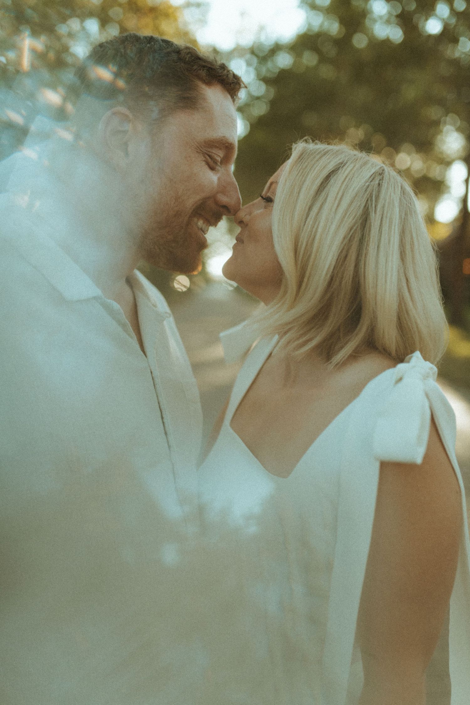 A romantic couple in white attire shares an intimate moment surrounded by dreamy smoke effects.