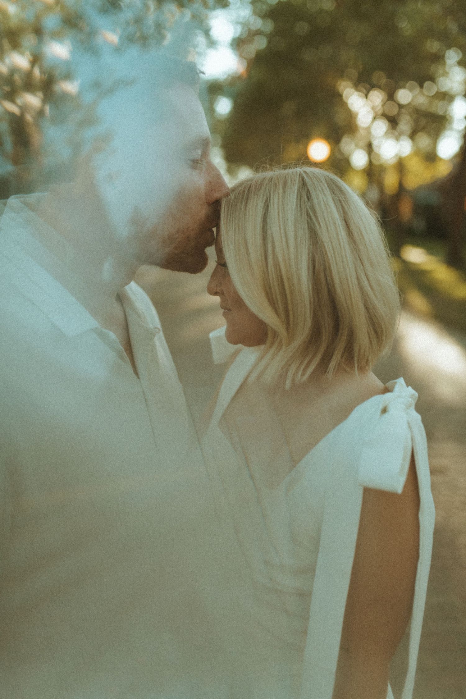 An intimate moment captured between a couple in white clothing during a sunset photoshoot.