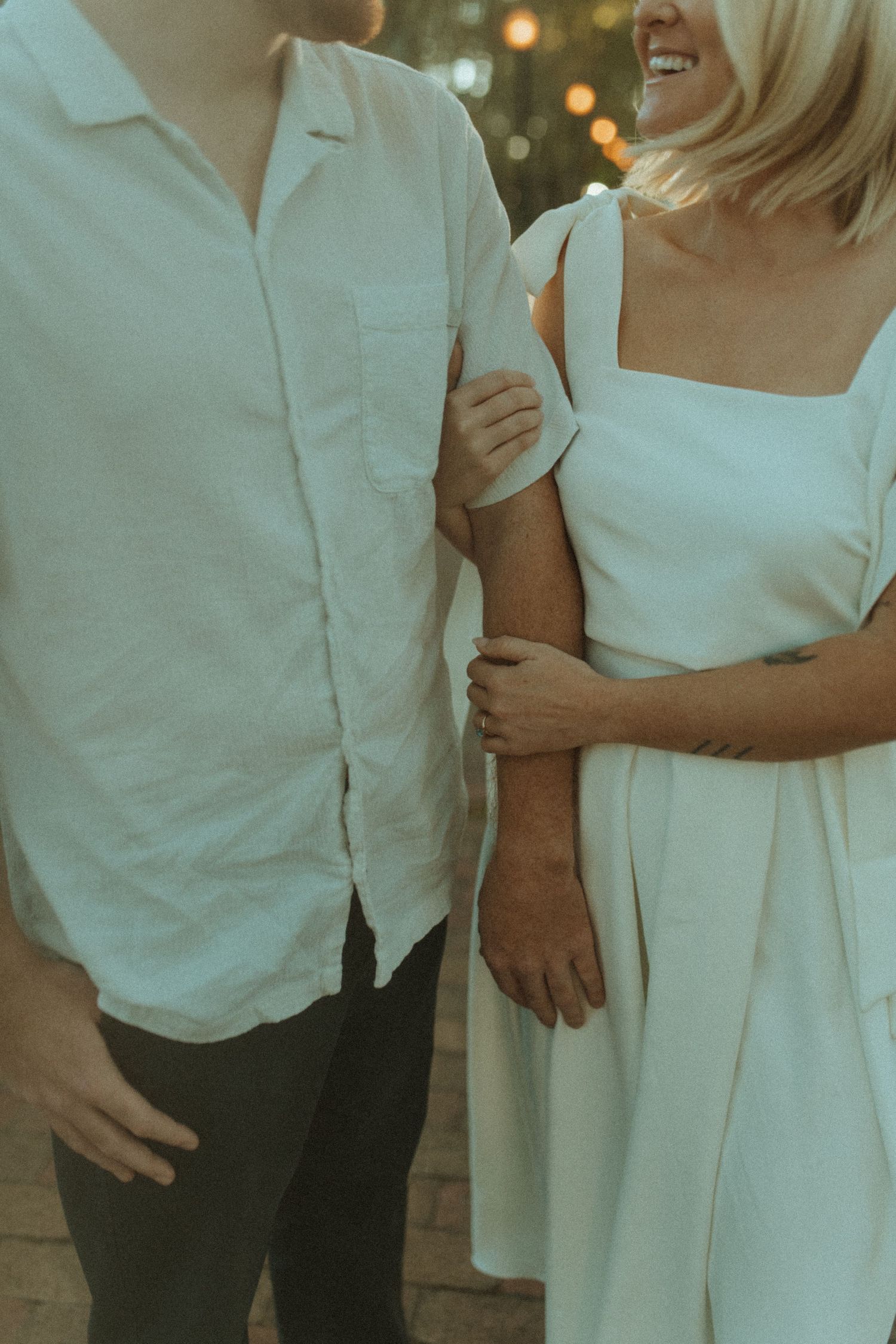 Close-up shot of couple in white outfits embracing on tree-lined street at sunset.